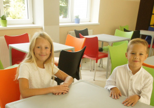 Uczniowie siedzący przy stole. W tle kolorowe krzesła i nowe stoliki.